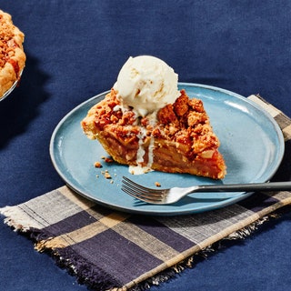 A slice of apple crumb pie on a plate topped with a scoop of drippy vanilla ice cream.