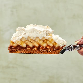 Side view of a slice of banoffee pie with a peanut caramel shingled banana slices and a mound of cream balanced on a pie...